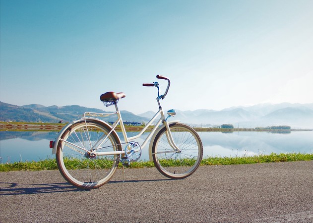 Vintage cream bicycle parked on a paved lakeside path with mountains reflected in calm water